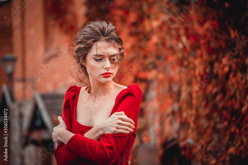 Portrait of Beautiful girl in a burgundy and red dress on a background of autumn grape leaves in the park, October