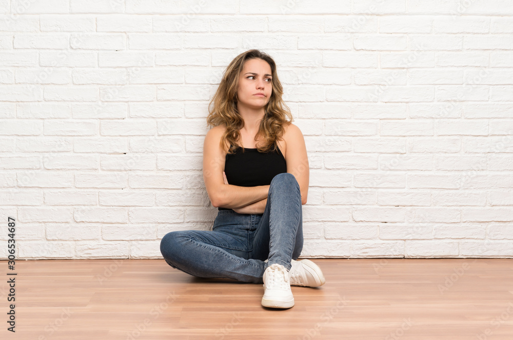 Young blonde woman sitting on the floor thinking an idea Young blonde woman sitting on the floor thinking an idea