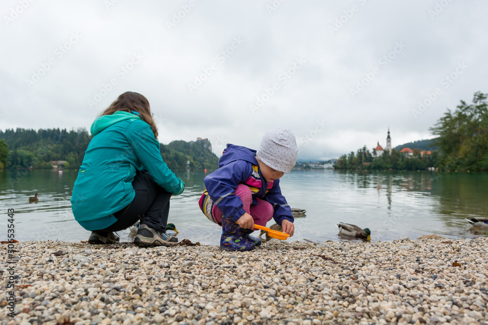 Mother and daughter playing on lake shore with romantic church in the bacground.