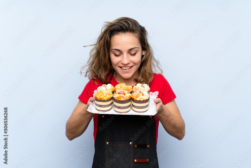 Young blonde woman holding mini cakes enjoying the smell of them