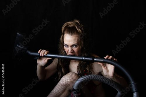 tired sexy girl holding a vacuum cleaner in her hands sitting next to him. Erotic cleaning.