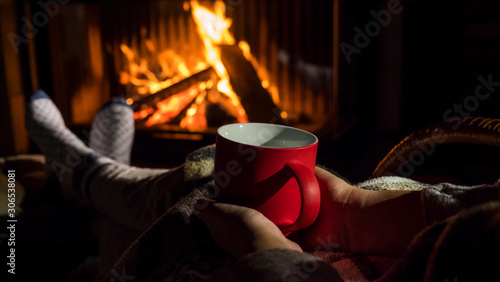 Woman with a red cup of tea is relaxing by the fireplace