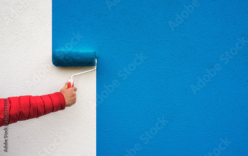 hand holds paint roller and painting a wall