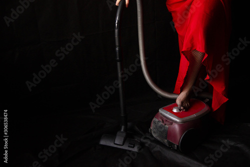 the girl in the red long dress is vacuuming. the leg in stockings presses the power button on the vacuum cleaner