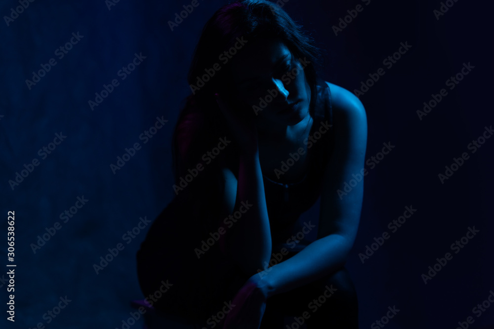 studio portrait of a girl in the light of blue and magenta neon lights. sad sits on a chair