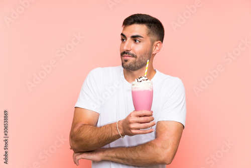 Young man with strawberry milkshake over isolated pink background making doubts gesture while lifting the shoulders