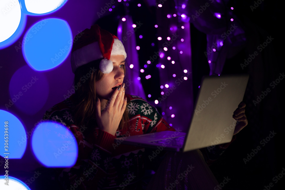 young girl with a laptop in the New Year sits at home in Christmas clothes, a woman buys gifts online for Christmas young girl with a laptop in the New Year sits at home in Christmas clothes, a woman buys gifts online for Christmas