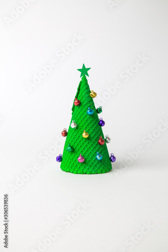 Green ice cream cone in form of Christmas tree decorated with colorful baubles and star on white background minimal creative holiday and food concept.