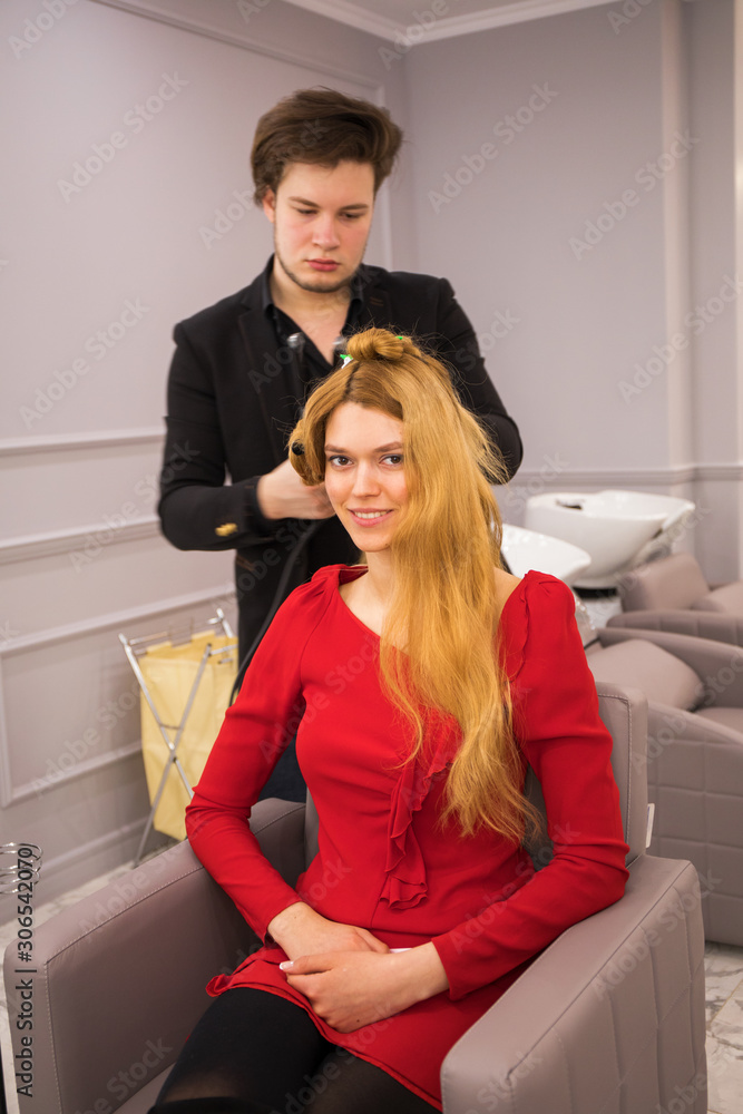 Obraz premium Male hairdresser styling hair for young beautiful woman