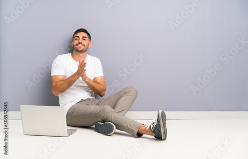 Young man with his laptop sitting one the floor applauding