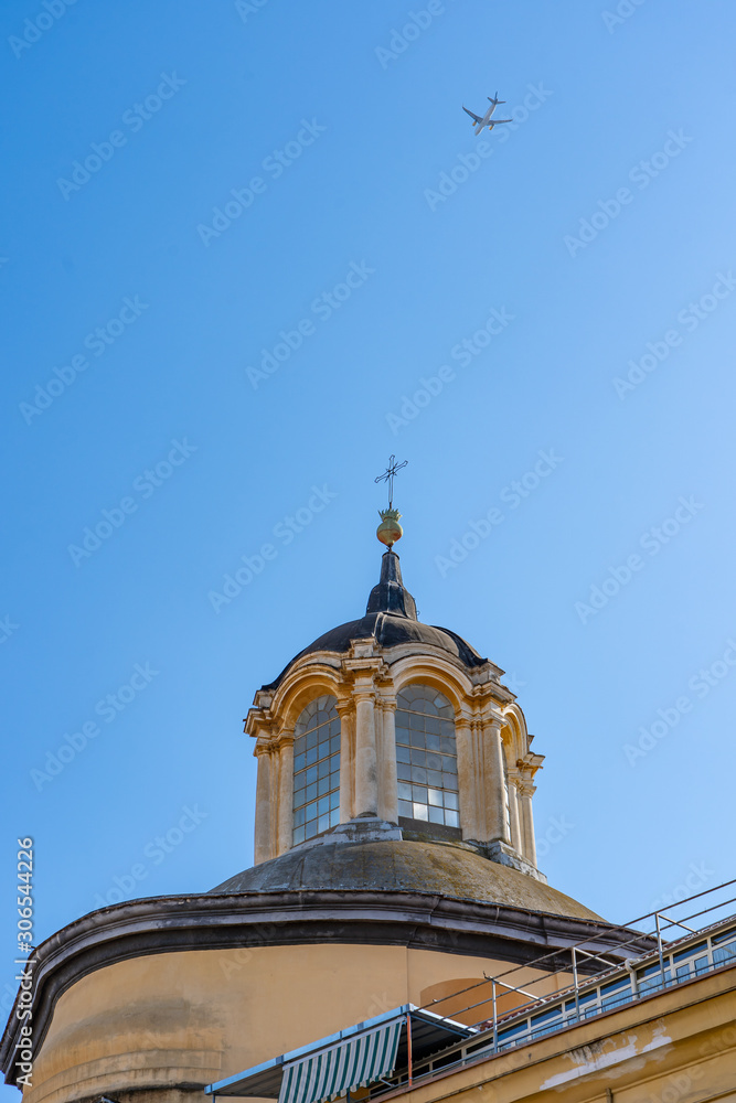 Plane in blue sky fly over church on the street of Naples