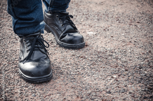 Man wearing safety shoes black color, standing on the ground © Sawat