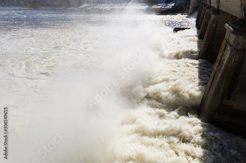 Water drains from the reservoir creating pillars of water vapor and foam. A hydroelectric power station generates electricity, draining excess water from reservoir into a river. Waterfall on the river