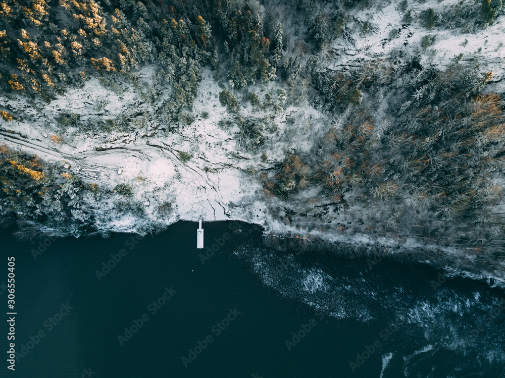 Aerial view of wooden pier in  forest by the blue lake in rural winter Finland landscape
