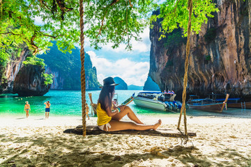 Traveler woman in bikini sitting on swing using tablet on tropical beach Lao Lading island Krabi, Leisure tourist travel Phuket Thailand Summer holiday vacation, Tourism beautiful destination Asia