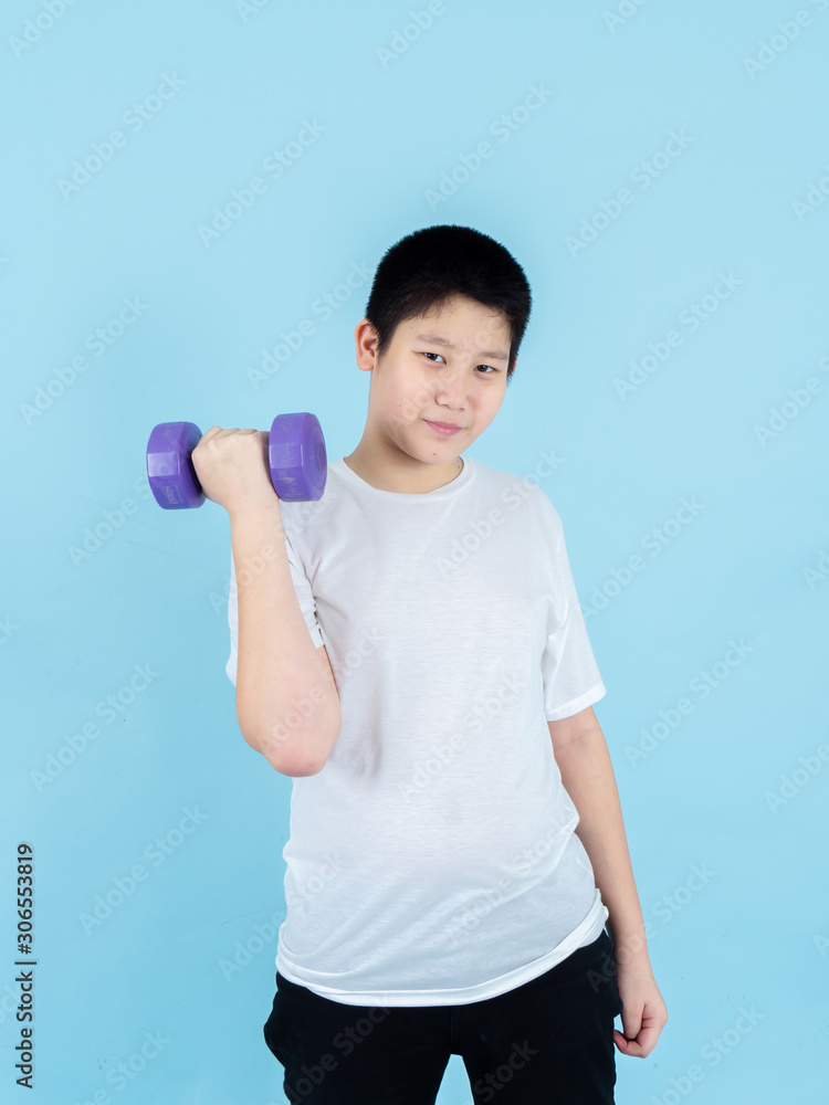 Smiling Asian boy using dumbbell on blue background. Smiling Asian boy using dumbbell on blue background.