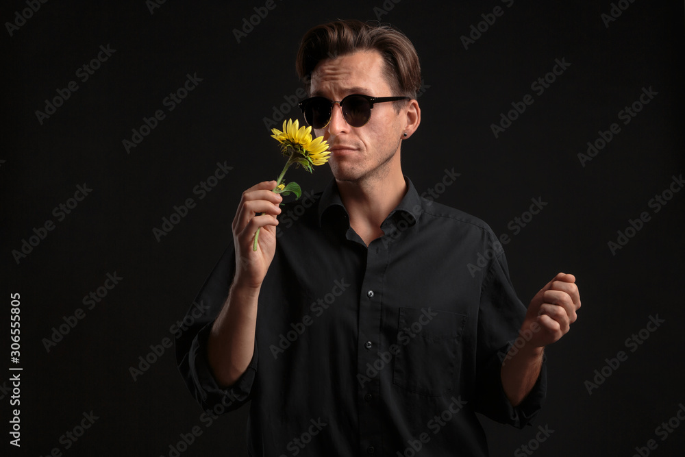 Handsome man in a black shirt and sunglasses holding beautiful yellow flower Handsome man in a black shirt and sunglasses holding beautiful yellow flower
