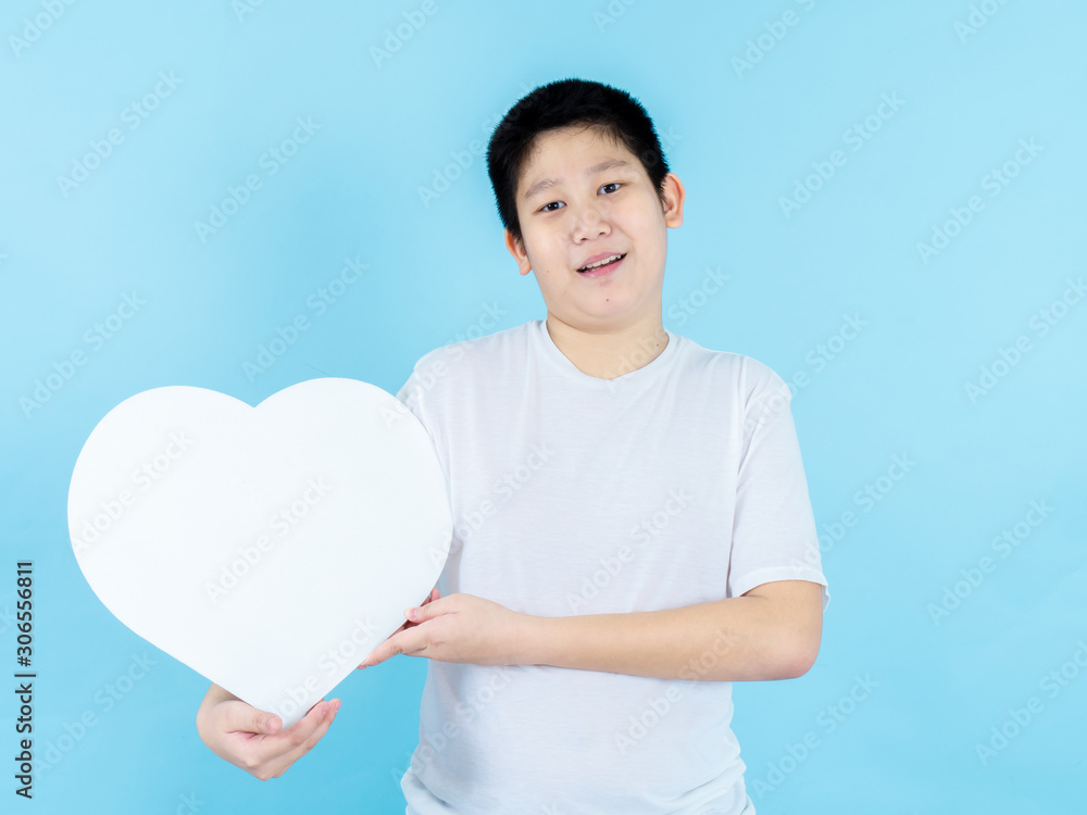 Asian preteen boy holding white heart shape speech bubble on blue background. Asian preteen boy holding white heart shape speech bubble on blue background.