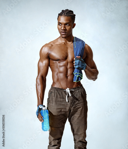 Tired man resting after training. Photo of sporty man with towel on shoulders holds bottle of refreshing water on grey background. Resting time. Health concept.