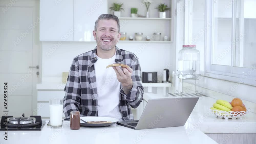 Caucasian man laughing and smiling at the camera while holding a bread with chocolate cream in the kitchen. Shot in 4k resolution Caucasian man laughing and smiling at the camera while holding a bread with chocolate cream in the kitchen. Shot in 4k resolution
