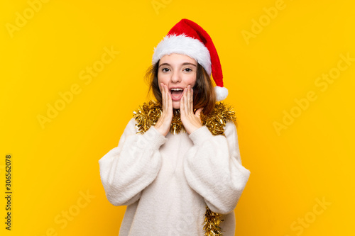 Girl with christmas hat over isolated yellow background with surprise facial expression
