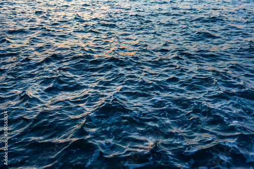 Fotografie, Obraz Dark blue Sea water with a choppy  texture and reflected orange highlights from