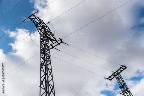 Torres de electricidad conectadas por cables con el cielo azul y con nubes de fondo.