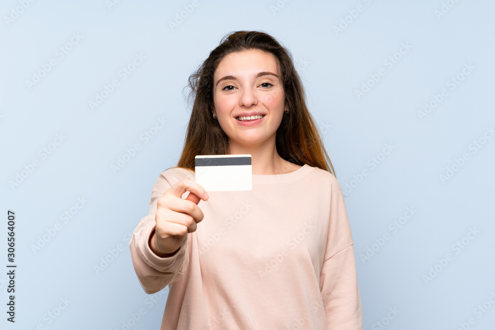 Young brunette girl over isolated blue background holding a credit card Young brunette girl over isolated blue background holding a credit card