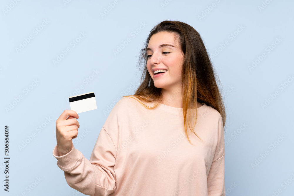 Young brunette girl over isolated blue background holding a credit card Young brunette girl over isolated blue background holding a credit card