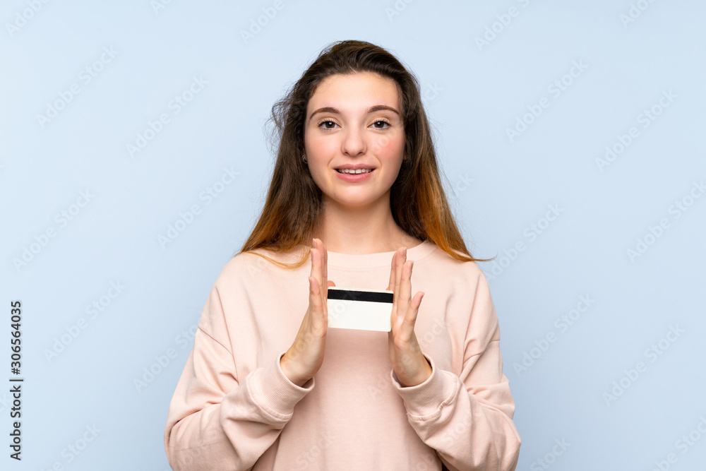 Young brunette girl over isolated blue background holding a credit card Young brunette girl over isolated blue background holding a credit card