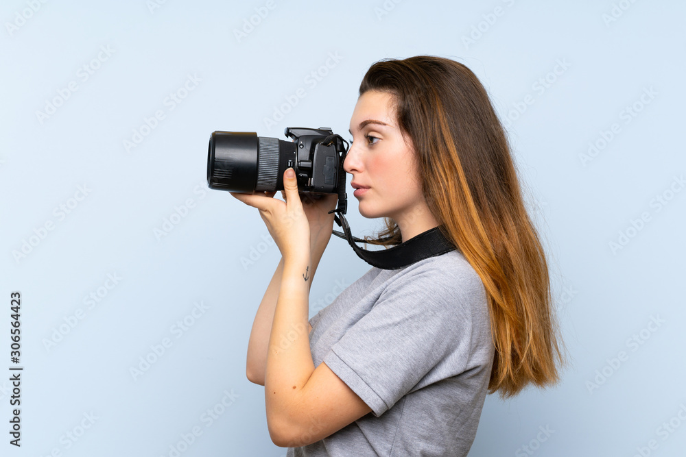 Young brunette girl over isolated blue background with a professional camera Young brunette girl over isolated blue background with a professional camera