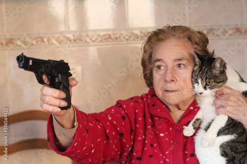 Angry senior woman protecting her cat with a gun  photo