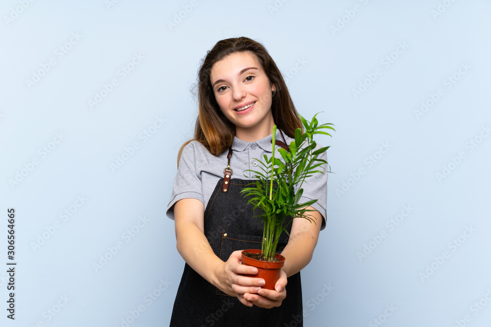 Young brunette girl over isolated blue background taking a flowerpot Young brunette girl over isolated blue background taking a flowerpot