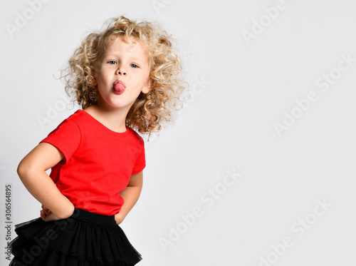 Frolic little kid girl in black fatin skirts and red t-shirts is holding hands on hips, sticking her tongue out at us