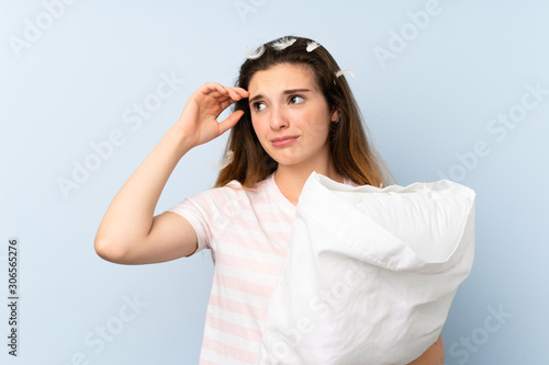 Young woman in pajamas over isolated blue background having doubts and with confuse face expression