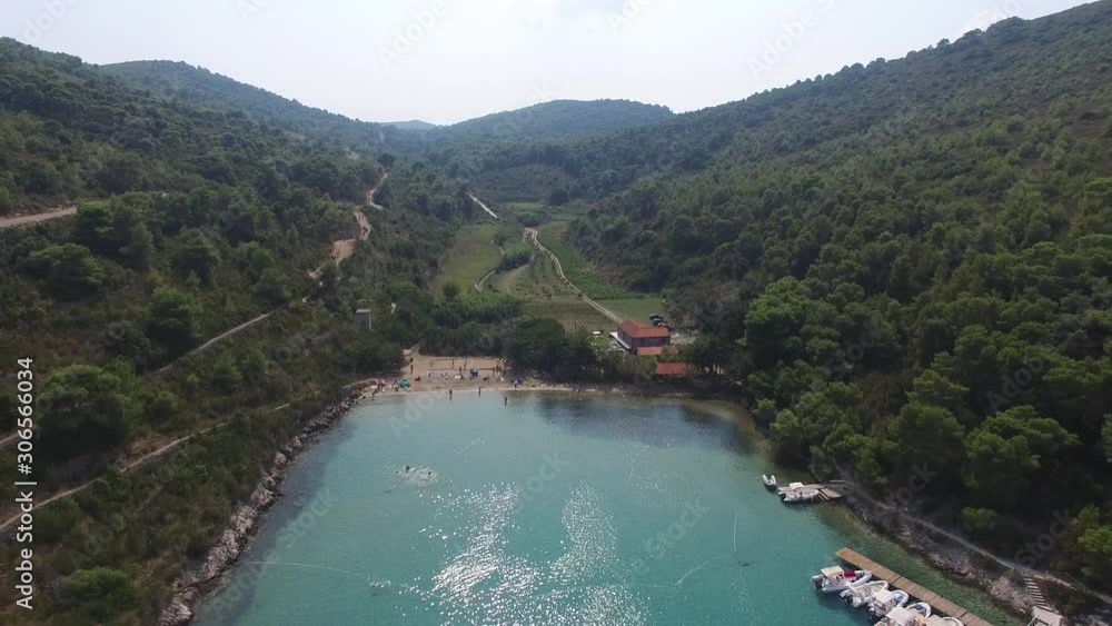 Scenic hillside and valley leading to a small bay with sailboats in clear blue water, beach with people playing and sunbathing. Aerial view, drone backing. Scenic hillside and valley leading to a small bay with sailboats in clear blue water, beach with people playing and sunbathing. Aerial view, drone backing.