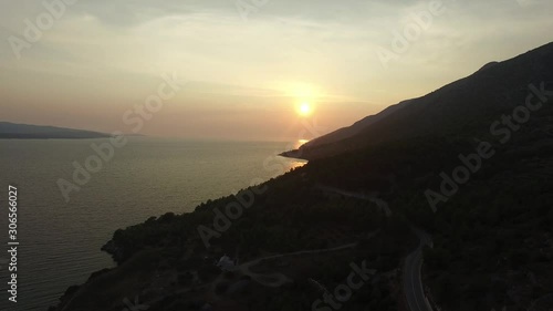 Aerial view from drone backing reveals amazing sunset over the ocean and a small island of Croatia. Long narrow road leads toward the setting sun.