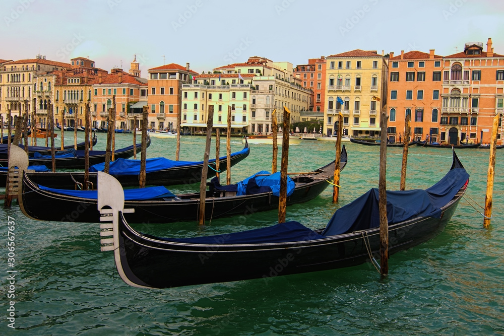 Venice, Italy-September 28, 2019: Classic landscape of Venice. Old black gondolas moored near wooden mooring poles. Scenic Grand Canal with turquoise water with ancient colorful buildings