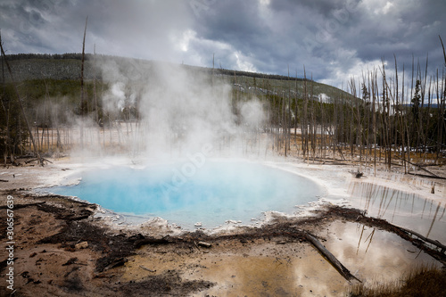 Blue geyser basin with smoke boiling in dry environment.