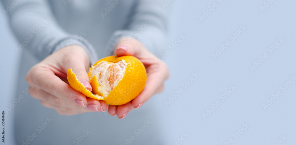 Woman holding and cleans tangerine on gray light background, space for text Woman holding and cleans tangerine on gray light background, space for text