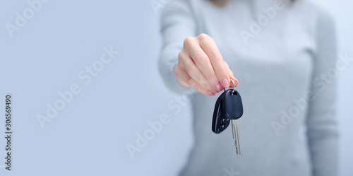 Woman holding car key on gray light background  space for text