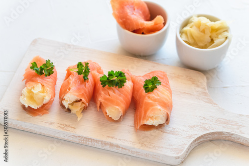 Slices of smoked salmon wrapped with cottage cheese and marinated ginger. Party snack.