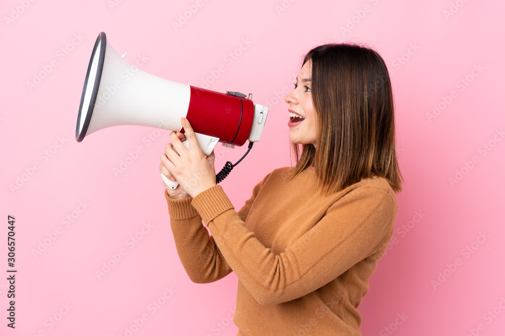 Young woman over isolated pink background shouting through a megaphone