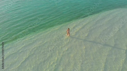 4K aerial view of a woman walking alone to the pier with wooden arbors on isolated white sandbar in Onok island in Balabac, Philippines photo