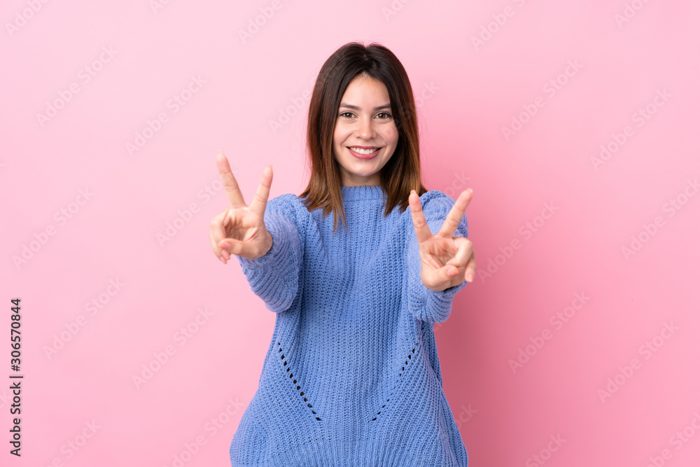 Young woman with blue sweater over isolated pink background smiling and showing victory sign Young woman with blue sweater over isolated pink background smiling and showing victory sign