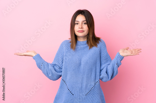 Young woman with blue sweater over isolated pink background having doubts with confuse face expression