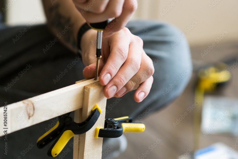 Man, carpenter using a screwdriver during woodwork, closeup on hands