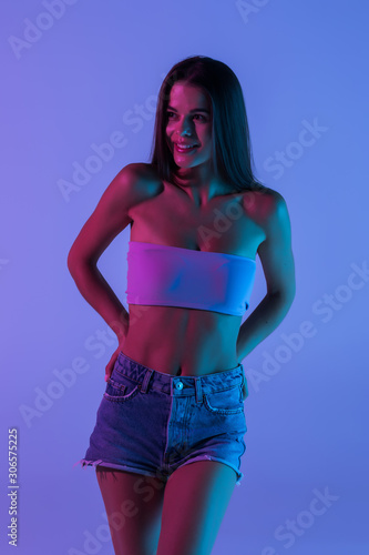 Young pretty girl in denim shorts and cropped top on a violet light background