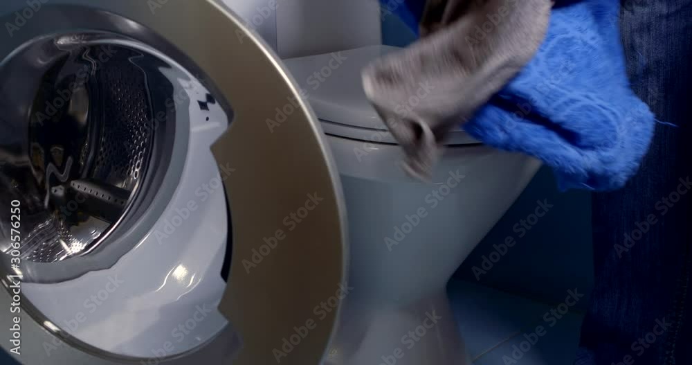 man is putting dirty laundry inside drum of washing machine in home bathroom man is putting dirty laundry inside drum of washing machine in home bathroom