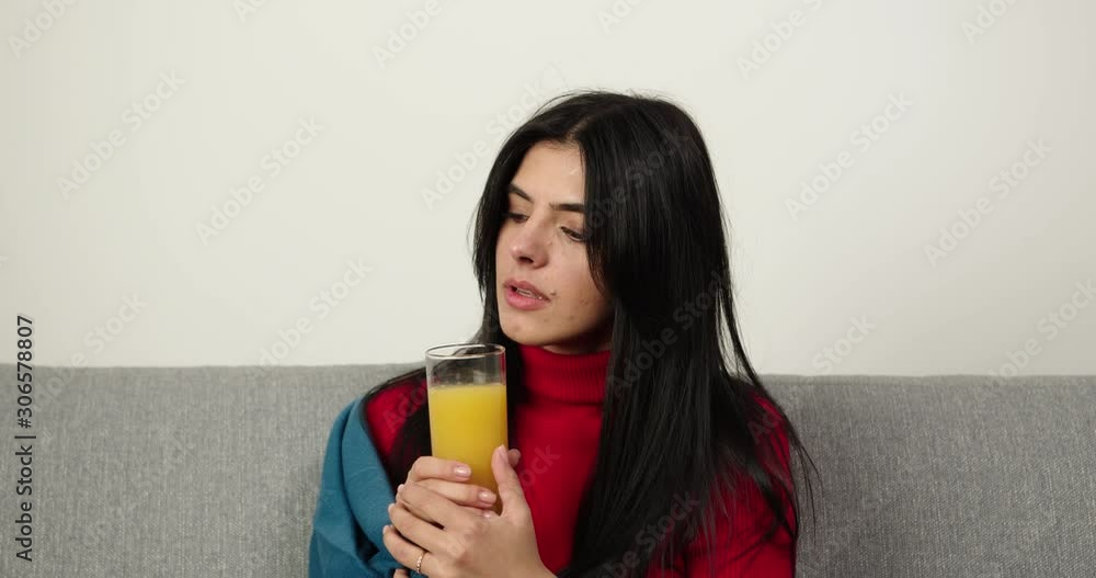 Brunette sitting on the sofa with warm plaid and drink glass of juice. Girl is frozen .Іndoor Brunette sitting on the sofa with warm plaid and drink glass of juice. Girl is frozen .Іndoor